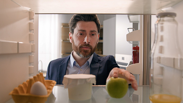 Man in a suit looking into an office fridge, representing a coworker taking coworker's lunches.