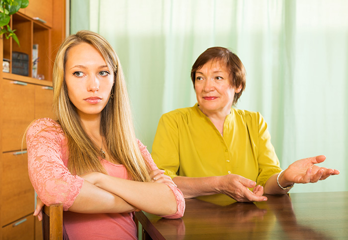 An upset young woman sitting at a table ignoring an older woman explaining something, showing mom's favorite daughter context. An upset young woman sitting at a table ignoring an older woman explaining something, showing mom's favorite daughter context.