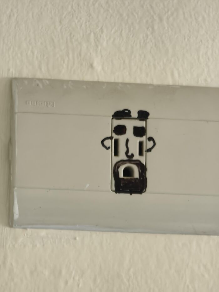 A wall power outlet drawn with marker to look like a face, creating an absurd moment.