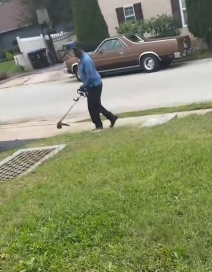 A neighbor trimming the grass edge along a driveway with a weed eater. A neighbor trimming the grass edge along a driveway with a weed eater.