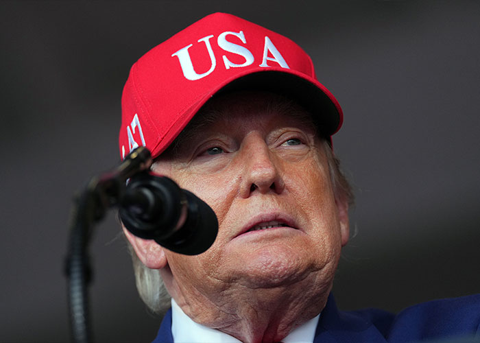 Close up of Donald Trump wearing a red USA hat speaking into a microphone, related to Trump waving at nobody news. Close up of Donald Trump wearing a red USA hat speaking into a microphone, related to Trump waving at nobody news.