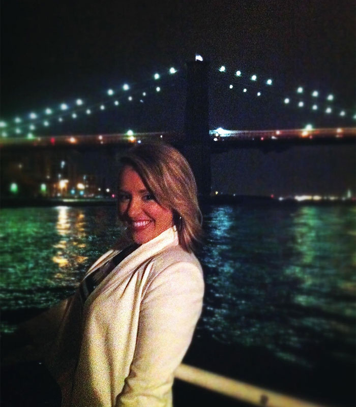 Female Amazon employee posing outdoors near a illuminated bridge at night.