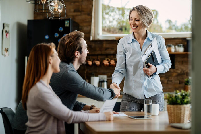 A real estate agent shaking hands with a couple indoors, related to cults recruiting.