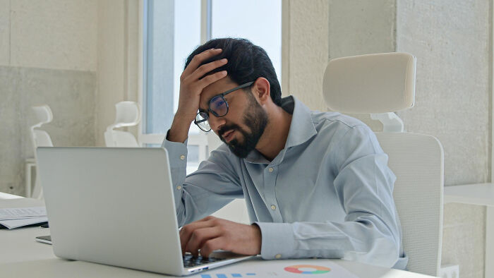 An overwhelmed office worker holding his head, showcasing people share breaking point moments.