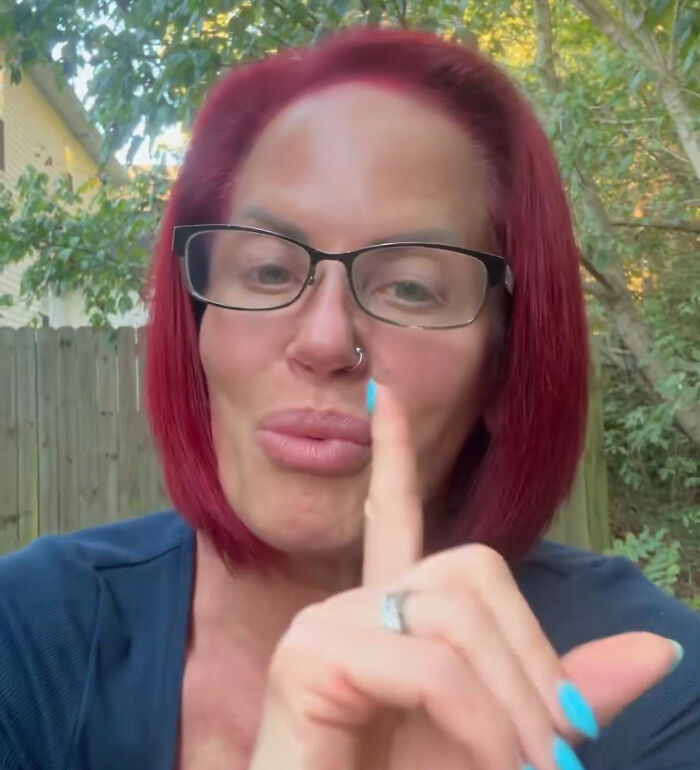 58 years old MAGA influencer with red hair and glasses making a shushing gesture outdoors