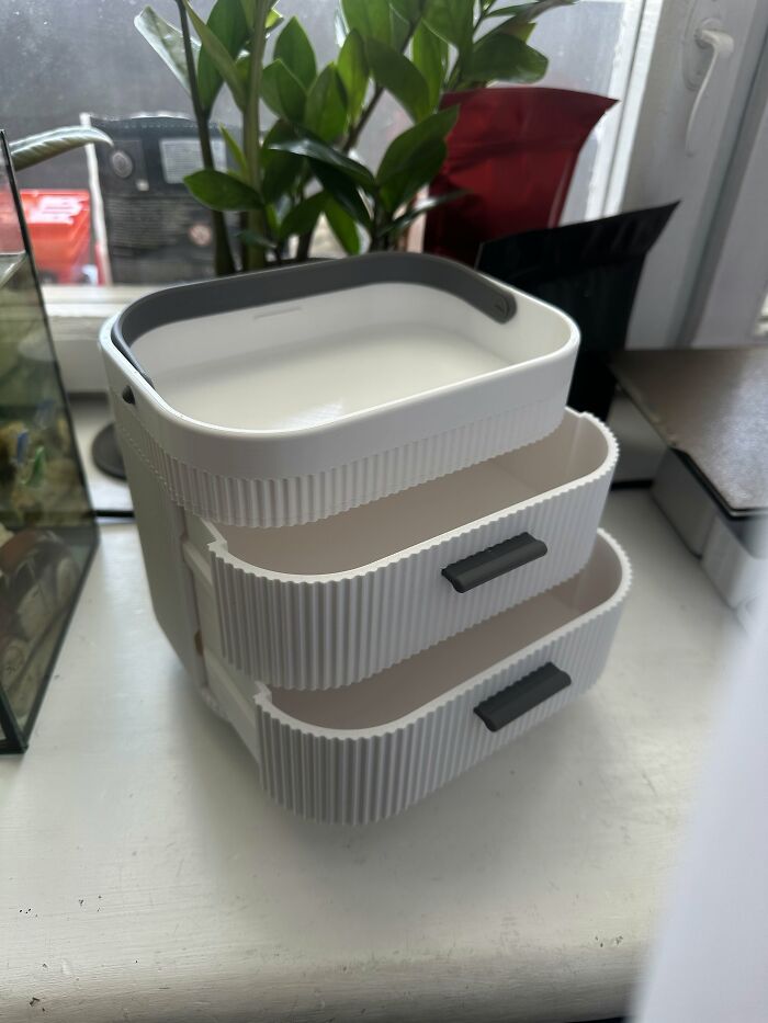 A white 3D prints mini organizer with small drawers next to a plant.