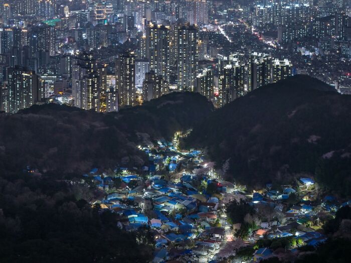 Aerial night landscape showing illuminated city buildings and a glowing village, from the Siena Drone Photo Awards.