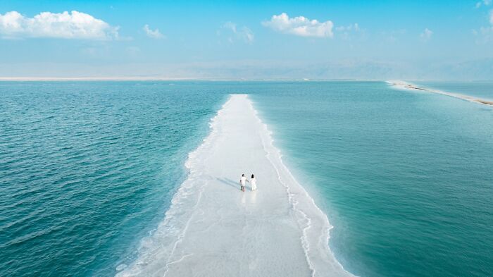 Top-down view of a couple walking along a white sandbar surrounded by turquoise water, from Siena Drone Photo Awards.