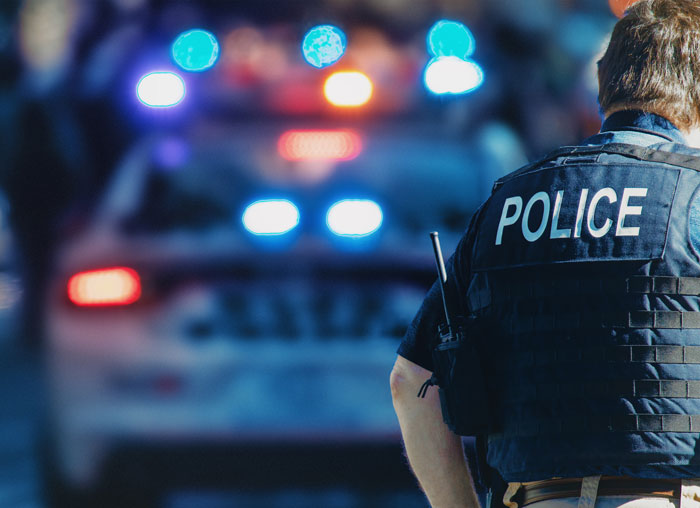 Police officer in tactical vest standing near patrol car after a drama involving a secret affair. Police officer in tactical vest standing near patrol car after a drama involving a secret affair.