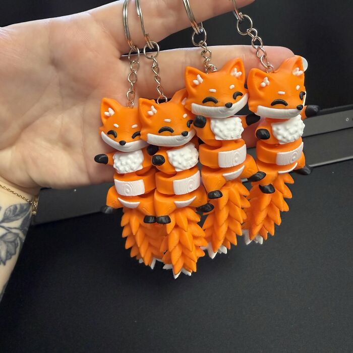 Four cute 3D prints of orange fox keychains held in a hand.