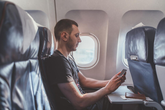 A male passenger looking at his phone while sitting in seats on flights