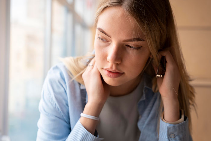 Pensive woman looking out a window while waiting for boyfriend gets heart surgery updates.
