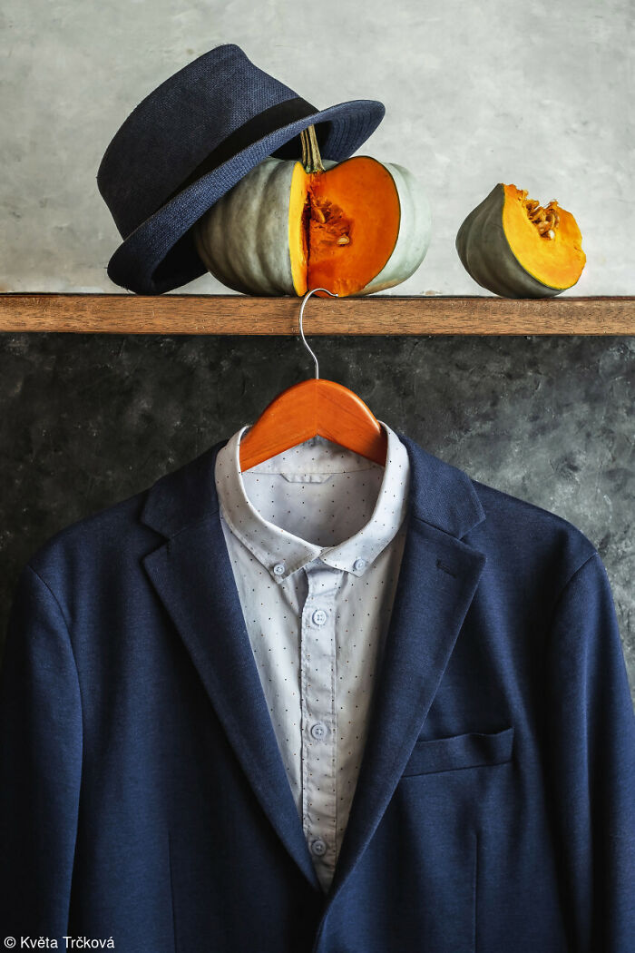 Blue jacket on a hanger with sliced grey and orange pumpkins and a fedora above