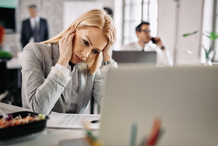 A stressed businesswoman sitting at her desk in front of a laptop while dealing with office drama.