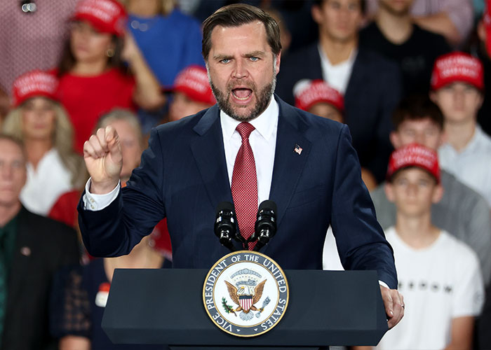Senator JD Vance speaking aggressively at a podium during a political rally. Senator JD Vance speaking aggressively at a podium during a political rally.