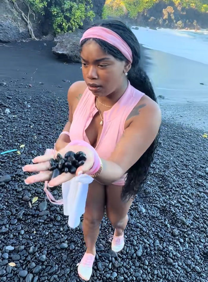 A tourist holds black sand and pebbles on a volcanic beach