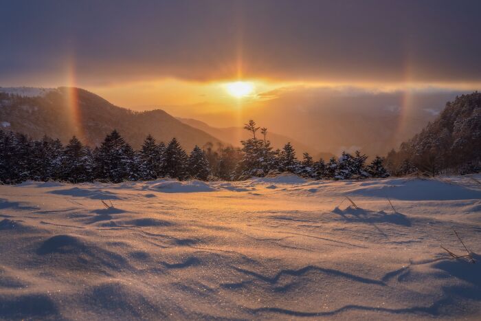 Natural landscape photography of a snow-covered mountain ridge under a vibrant winter sunset halo.