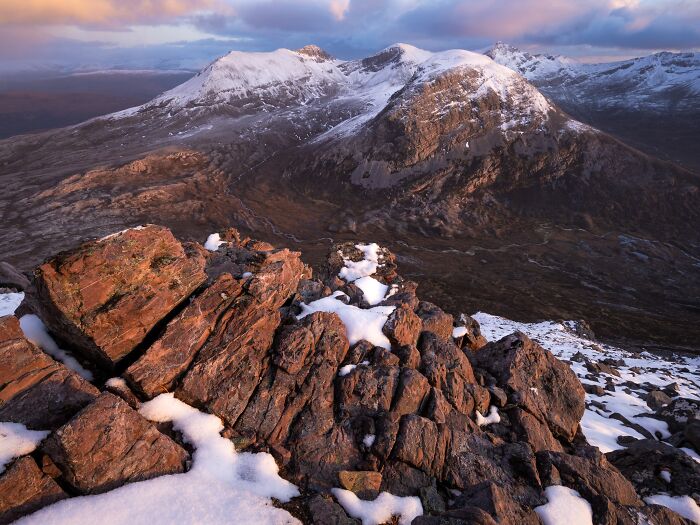 Dramatic mountain landscape photography with snow-capped peaks and rocky foreground at sunset