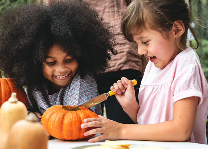 Two kids carving a pumpkin, which can be a Halloween activity that leads to a life-threatening illness.