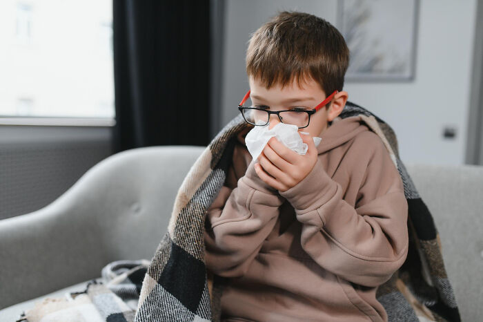 Sick boy blowing nose under blanket at home during the scariest moments of illness