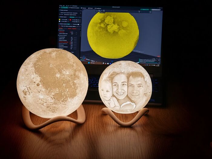 Two glowing spherical moon lamps on a table in front of a laptop, demonstrating custom 3D prints