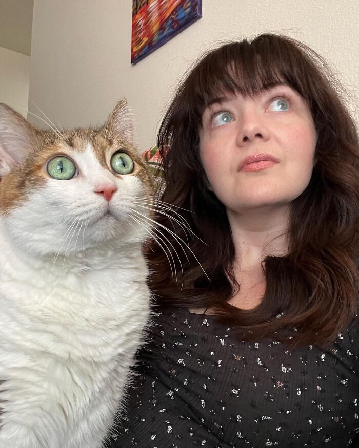 Woman and her pet cat looking upward with matching wide green eyes, showing how pets look like their owners.