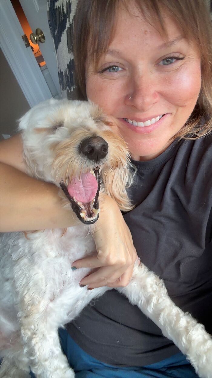 Smiling woman hugging her happy yawning pet dog