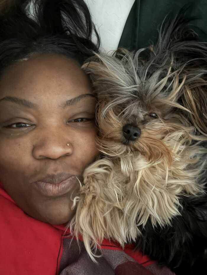 A smiling woman lying next to her fluffy, messy-haired small dog showing pets look like their owners.