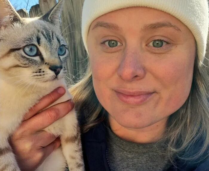 A woman with striking blue eyes posing next to her blue-eyed cat, showing how pets look like their owners.