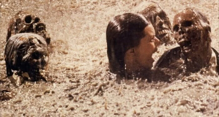 A woman screaming in muddy water with movie props skeletons from Poltergeist