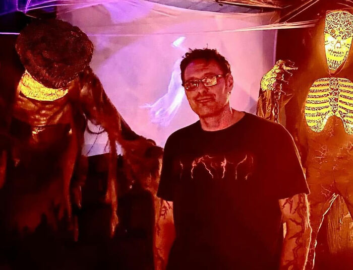 Man standing next to epic Halloween display with skeleton and spooky figures Man standing next to epic Halloween display with skeleton and spooky figures