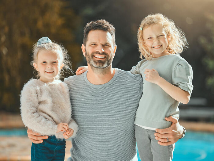 A smiling father hugging his two young daughters, representing the support students need against infuriating teachers
