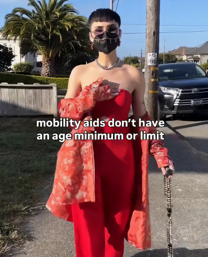 A young woman in a stylish red outfit walking with a embellished cane as a mobility aid.
