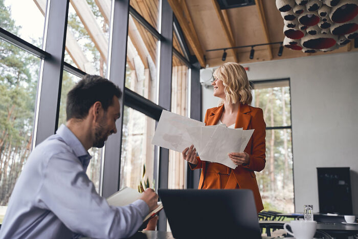 A smiling businesswoman holding papers near a colleague, depicting obvious lies in the workplace