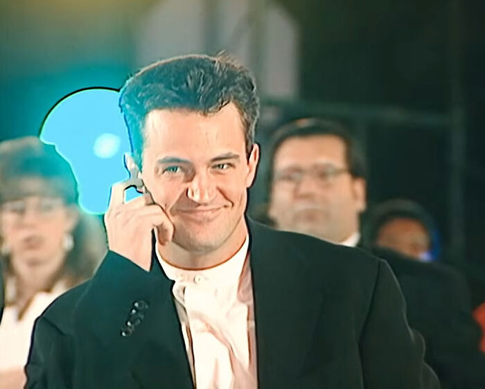 Actor Matthew Perry smiling while holding an earpiece at an event