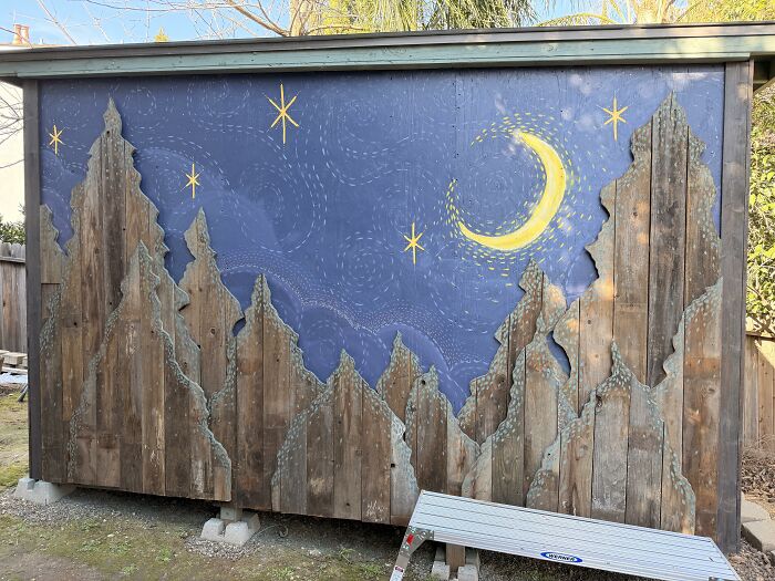 Outbuilding wall decorated with wooden pine tree cutouts and night sky painting, using creativity to save money.