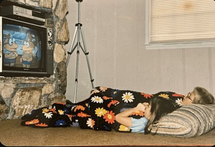 Children lying under a floral blanket watching cartoons on television, captured in nostalgic photos of 80s kids.