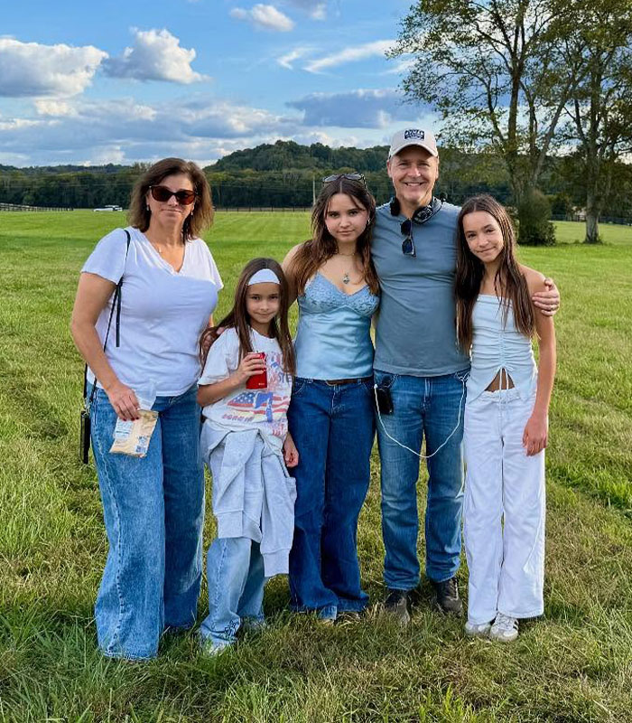 Chad Lowe stands with his wife and daughters in a green grassy field during a family outing.