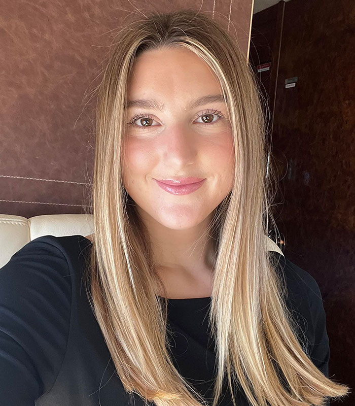 A young blonde flight attendant smiles warmly inside a luxury private jet.