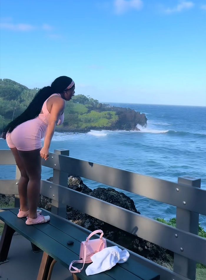 A tourist looks over the ocean from a wooden bench