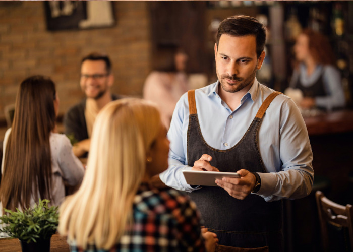 Waiter providing European customer service to a guest seated at a restaurant table Waiter providing European customer service to a guest seated at a restaurant table