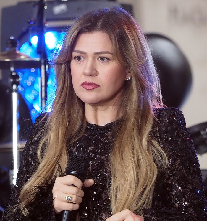 Kelly Clarkson holding a microphone with expressive body language on stage