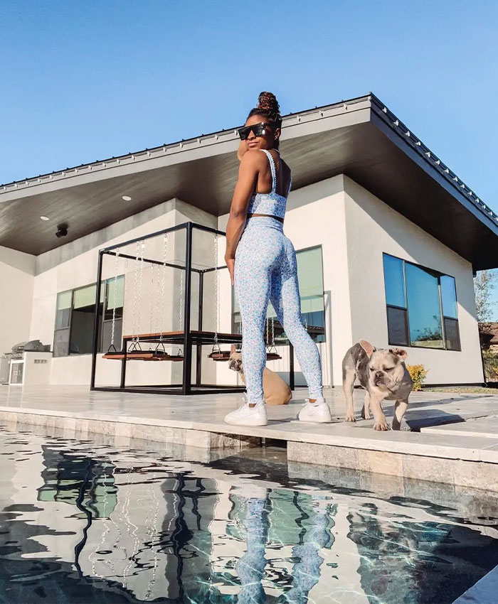 Simone Biles standing poolside with her dogs outside her modern Texas home.