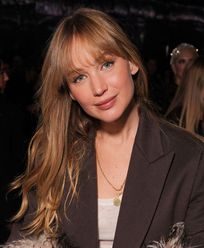 Jennifer Lawrence with blonde bangs smiling, showcasing her natural look amidst plastic surgery rumors.