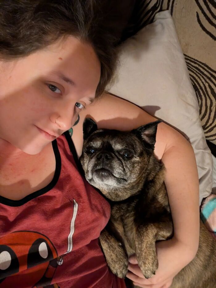 A woman smiling as she holds her small brindle pug dog close, sharing life stories with pets