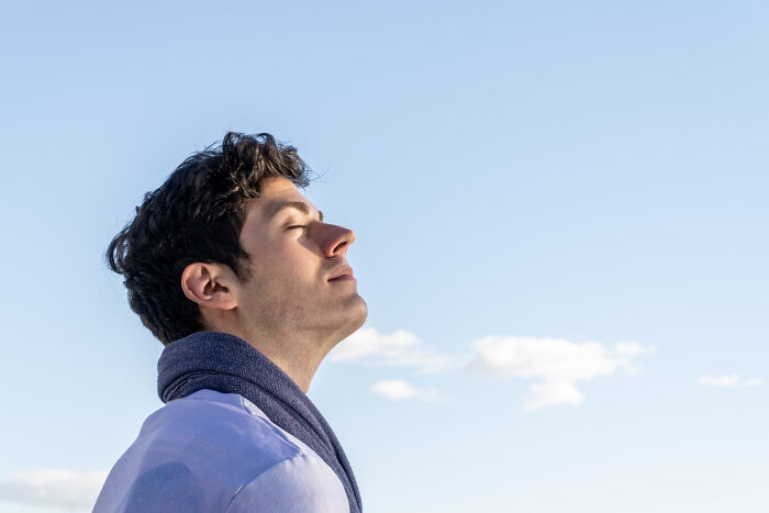 A young man looking up at the sky with eyes closed, embodying modern cults and belief systems