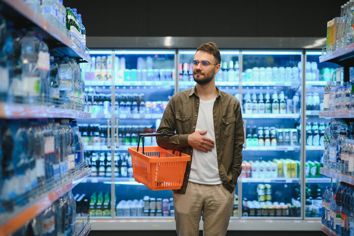 A confused man with a shopping basket in front of store coolers, relating to partners questioning intelligence