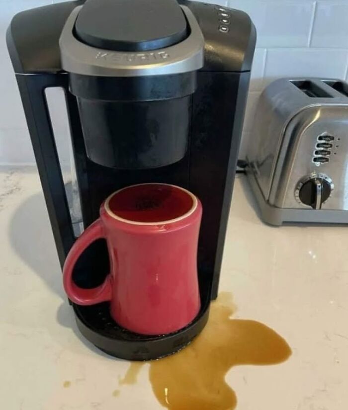 Absurd moment where spilled coffee sits next to an upside down mug under a coffee maker