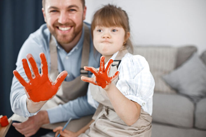 A smiling father and daughter with down syndrome showing orange painted hands during a fun art activity