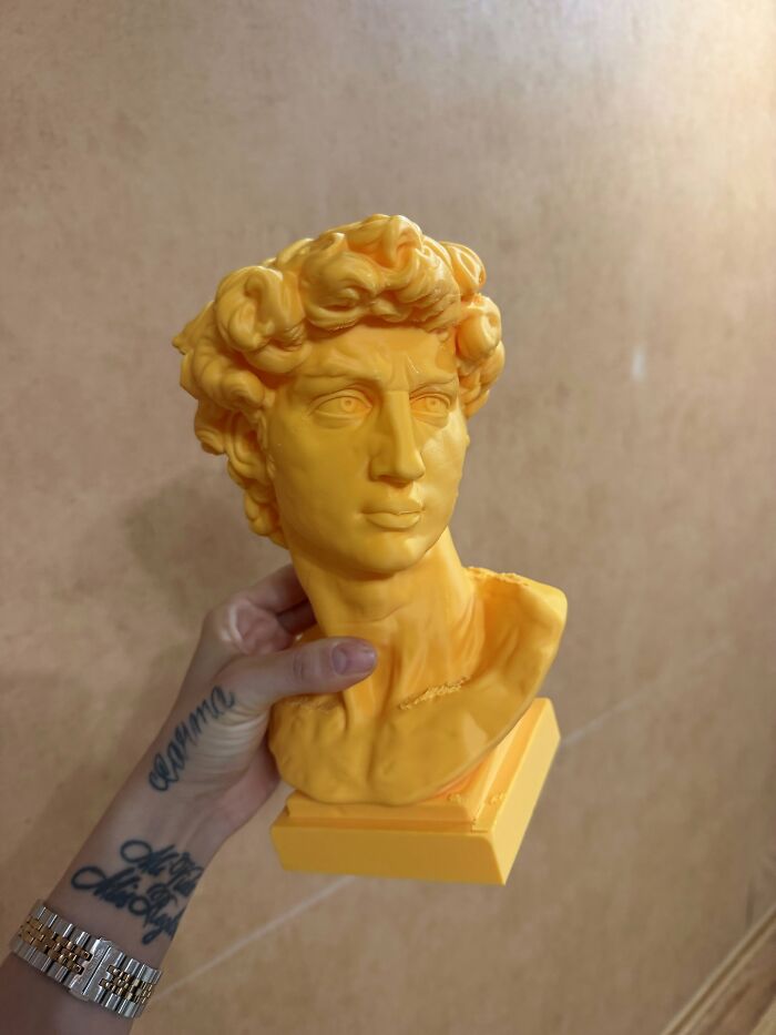 A vibrant yellow bust of David made from custom 3D prints being held in hand.